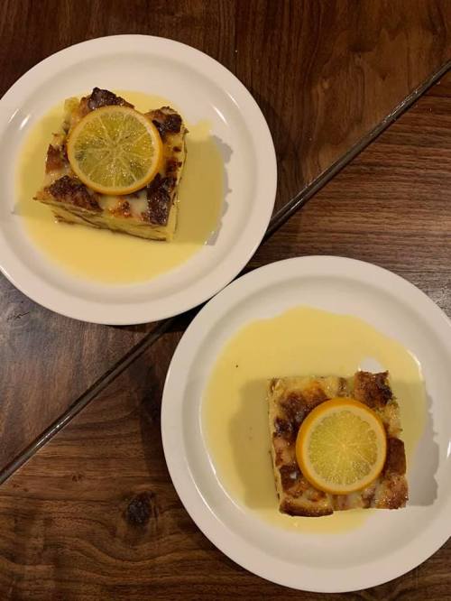 Two plates of dessert featuring a slice of cake topped with a lemon slice, served with a creamy sauce on a wooden table.