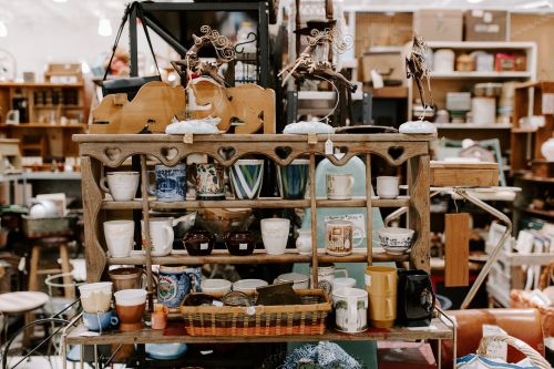 A wooden shelf filled with various cups, mugs, and decorative items in a vintage shop.