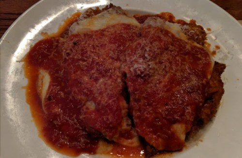 A plate of chicken parmesan topped with marinara sauce and melted cheese, served with a side of pasta.