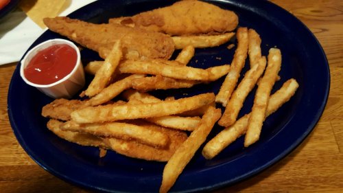 A blue plate with crispy fried chicken tenders and golden French fries, accompanied by a small cup of ketchup.