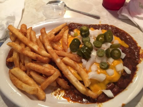 A plate of chili topped with cheese, onions, and jalapeños, served with a side of golden French fries.