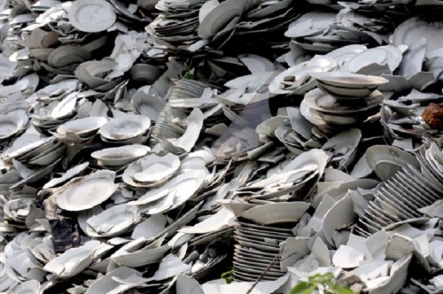 A large pile of stacked, discarded white plates in various sizes, creating a chaotic, textured surface.