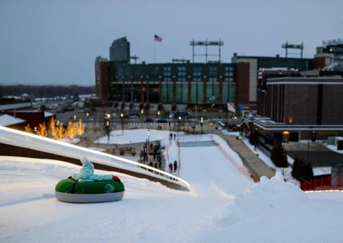 A snow tubing hill with a view of a stadium in the background, illuminated by lights at dusk.