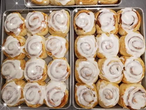 Freshly baked cinnamon rolls with creamy icing, arranged neatly in two trays, sparkling with a touch of shine.