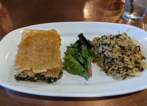 A plate with spinach pie, mixed greens, and a side of rice on a white dish.