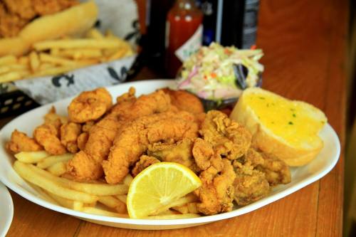 A plate of fried seafood, including shrimp and fish, served with fries, coleslaw, a slice of garlic bread, and lemon.