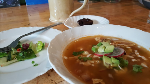 A bowl of soup with vegetables, a side salad, and a small dessert on a wooden table.