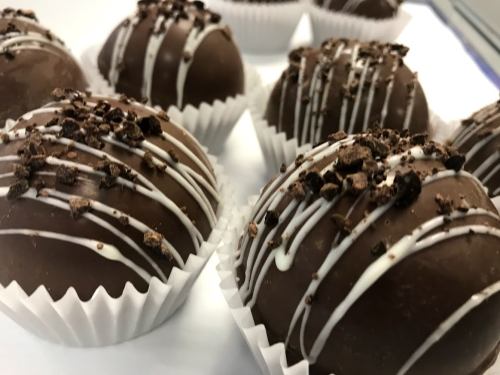 Close-up of chocolate truffles drizzled with white chocolate and topped with crushed cookies, arranged in paper cups.