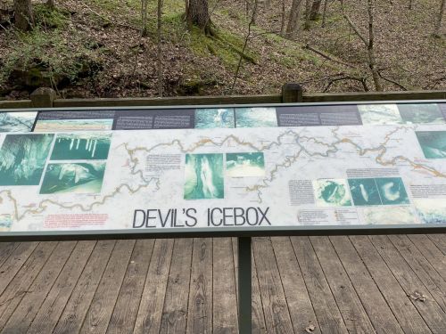 Information sign for Devil's Icebox, featuring maps and images of the cave system in a wooded area.