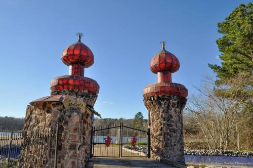 Entrance to McGee's Castle featuring two red domed towers and a stone gate, surrounded by trees and a lake.