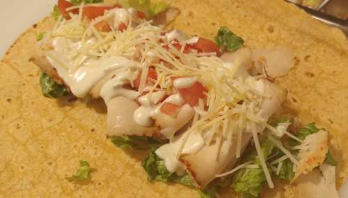 A tortilla filled with lettuce, sliced turkey, tomatoes, shredded cheese, and drizzled with mayonnaise.