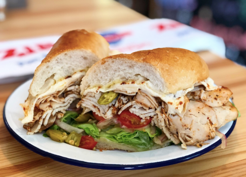 A hearty sandwich filled with sliced turkey, lettuce, tomatoes, and pickles, served on a toasted roll.