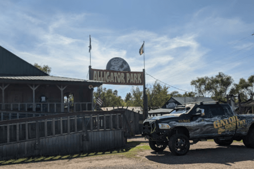 Sign for Alligator Park with a decorated truck parked nearby under a clear blue sky.