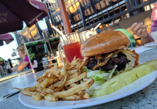 A juicy burger with lettuce and crispy onions, served with fries and a pickle on a plate at an outdoor dining setting.