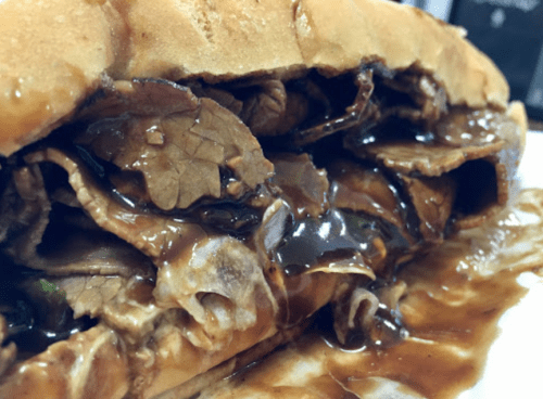 Close-up of a hearty sandwich filled with tender beef, drizzled with savory sauce, nestled in a soft roll.