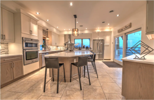 Modern kitchen with light cabinetry, a large island, bar stools, and large windows overlooking a scenic view.
