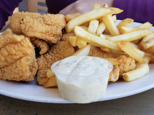 A plate of crispy fried chicken pieces served with golden French fries and a small cup of dipping sauce.