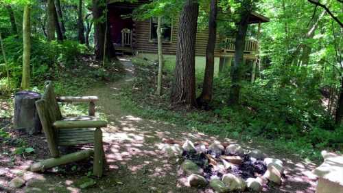 A serene forest path leading to a cabin, with a wooden bench and a fire pit surrounded by stones.