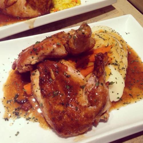 A plate of roasted chicken with a glossy sauce, served with mashed potatoes and carrots, garnished with herbs.