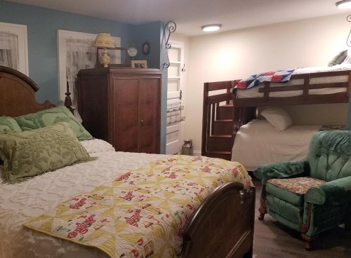 Cozy bedroom featuring a queen bed, bunk beds, a green armchair, and decorative quilts on the walls.