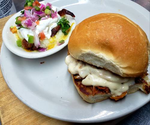 A sandwich with grilled chicken and creamy sauce, served with a side of loaded potato with toppings.