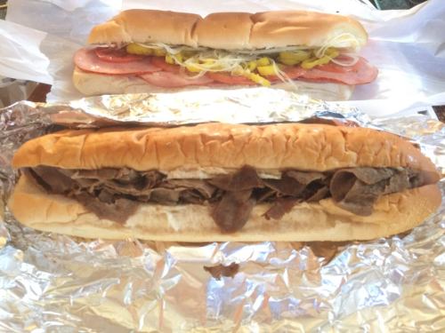 Two sandwiches: one with sliced meats and toppings, the other with shredded beef in a bun, wrapped in foil.