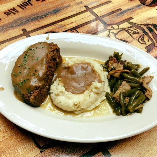 A plate featuring meatloaf with gravy, mashed potatoes, and green beans on a wooden table.