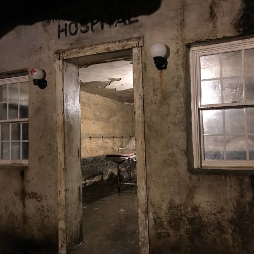 An eerie, dimly lit entrance to a rundown building labeled "HOSPITAL," with a gurney visible inside.
