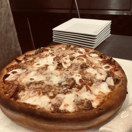 A freshly baked pizza with melted cheese and toppings, placed on a countertop near stacked white plates.