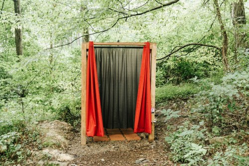 A wooden frame with red curtains stands in a lush green forest, creating a secluded space in nature.