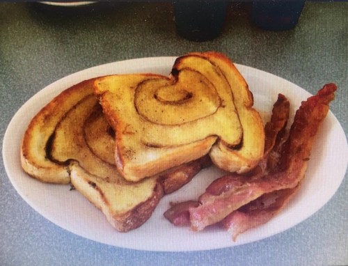 A plate with three slices of cinnamon swirl French toast and crispy bacon strips on the side.