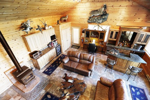 Cozy wooden cabin interior with leather sofas, a stone fireplace, and rustic decor featuring mounted animal heads.