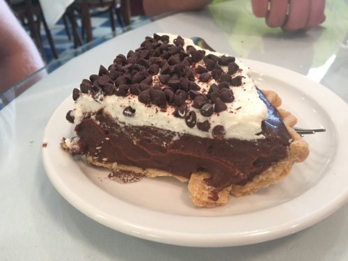 A slice of chocolate cream pie topped with whipped cream and chocolate chips on a white plate.