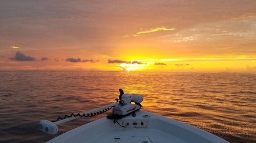 A boat's bow facing a vibrant sunset over calm waters, with clouds reflecting warm colors in the sky.