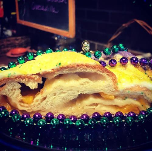 A close-up of a colorful king cake slice, filled with cream and topped with festive beads.