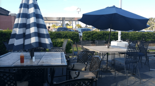 Outdoor dining area with metal tables and chairs, featuring a large blue umbrella and a checkered umbrella.