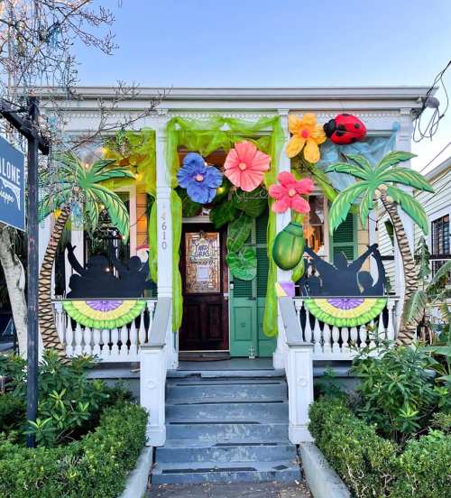 Colorful tropical decorations adorn a house entrance, featuring large flowers, greenery, and playful silhouettes.