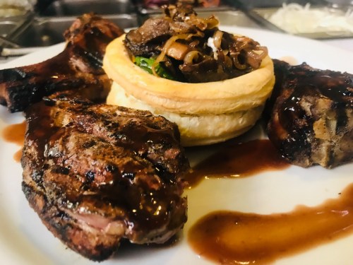 Grilled meat with a savory pastry filled with vegetables and sauce, served on a white plate.