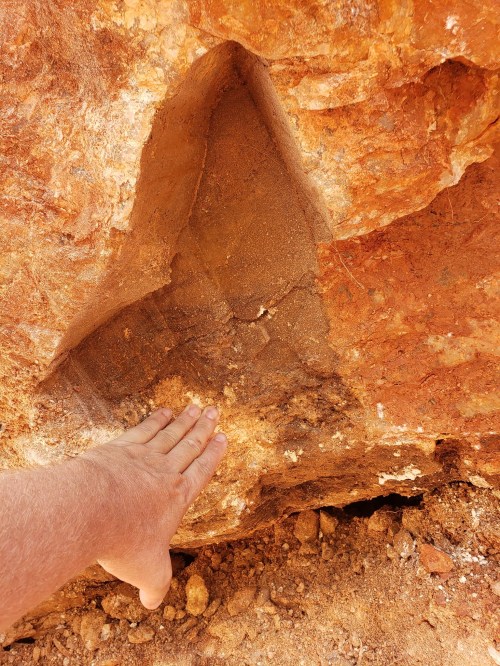 A hand rests on a textured rock surface with a triangular-shaped indentation in the stone.
