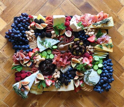 A colorful charcuterie board featuring fruits, cheeses, meats, nuts, and honey arranged artfully on a wooden surface.