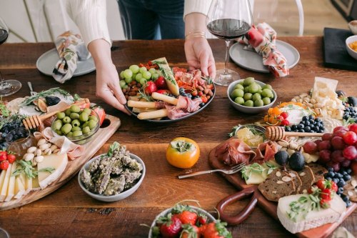 A beautifully arranged charcuterie spread with fruits, cheeses, meats, and wine on a wooden table.