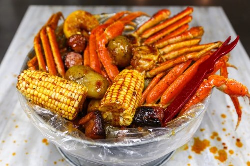 A large seafood boil featuring crab legs, corn, potatoes, sausage, and spices in a bucket.