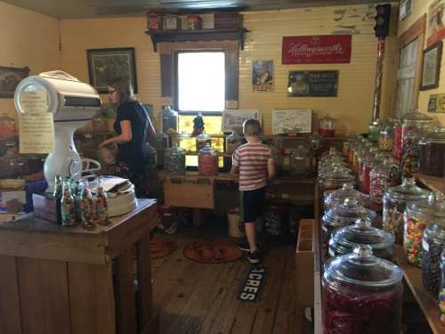 A vintage candy shop with jars of colorful sweets, a child exploring, and an adult organizing items in the background.
