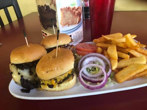 A plate with three mini burgers topped with cheese and onions, served with fries, lettuce, and tomato slices.
