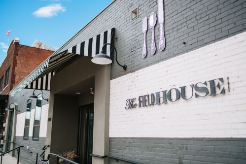 Exterior of The Fieldhouse restaurant, featuring a striped awning and modern signage on a brick wall.