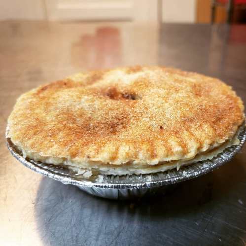 A freshly baked pie with a golden-brown crust, sitting in a silver pie tin on a metal surface.