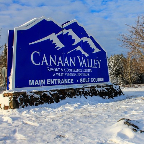 Sign for Canaan Valley Resort and Conference Center, featuring mountains, with snow-covered ground and a blue sky.