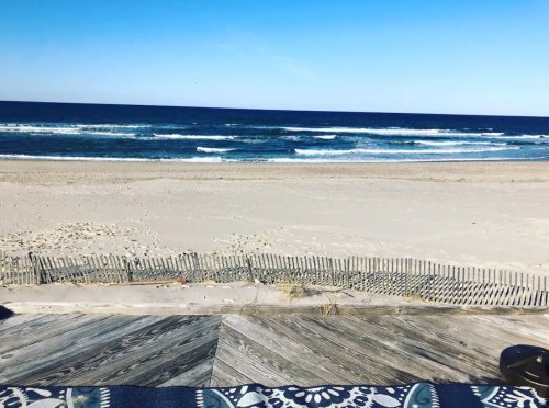 A serene beach view with gentle waves, sandy shore, and a clear blue sky.