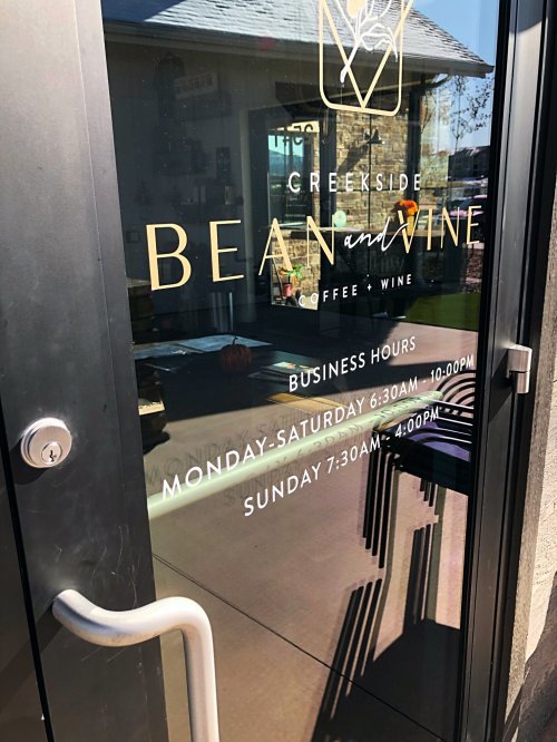 Glass door with "Creekside Bean and Wine" sign, listing business hours for coffee and wine.