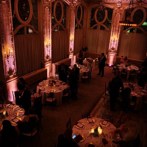 Elegant banquet hall with dim lighting, round tables set for dining, and guests mingling in a sophisticated atmosphere.